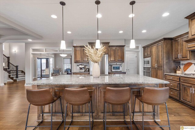 kitchen featuring a breakfast bar area, appliances with stainless steel finishes, light stone countertops, a large island with sink, and recessed lighting