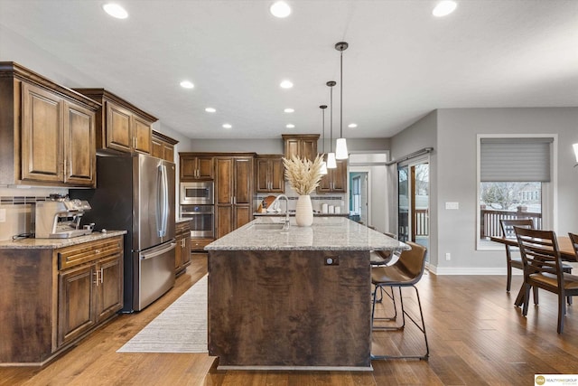kitchen featuring appliances with stainless steel finishes, light stone counters, recessed lighting, wood finished floors, and a center island with sink