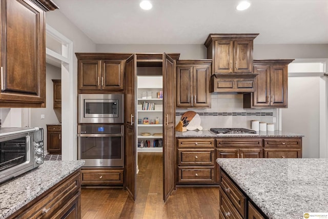kitchen featuring a toaster, appliances with stainless steel finishes, light stone countertops, and dark wood finished floors