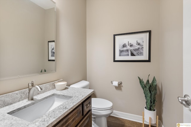 bathroom featuring vanity, baseboards, wood finished floors, and toilet