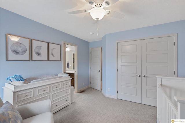 bedroom with a closet, ensuite bath, ceiling fan, light carpet, and baseboards