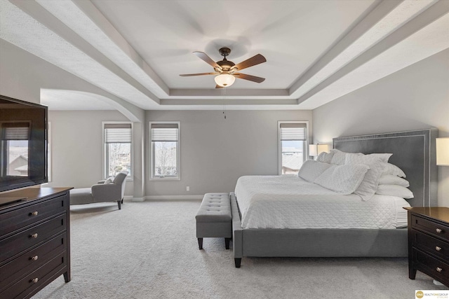 bedroom featuring a ceiling fan, arched walkways, baseboards, light carpet, and a tray ceiling