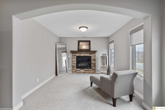 carpeted living area featuring baseboards and a stone fireplace