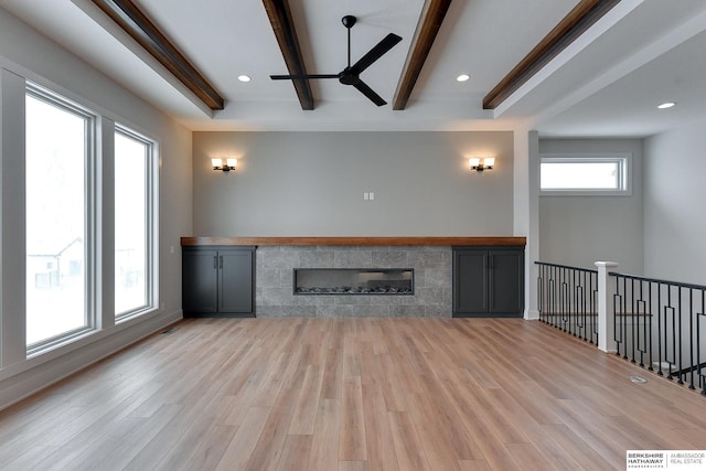 unfurnished living room featuring a glass covered fireplace, beamed ceiling, wood finished floors, and ceiling fan