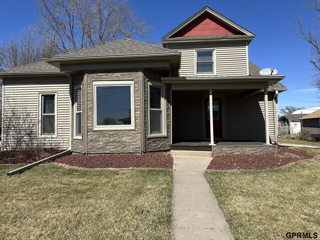 108 S Quince Ave, Dewitt, NE 68341 - view of front of home with stone siding, covered porch, a front yard, and a shingled roof