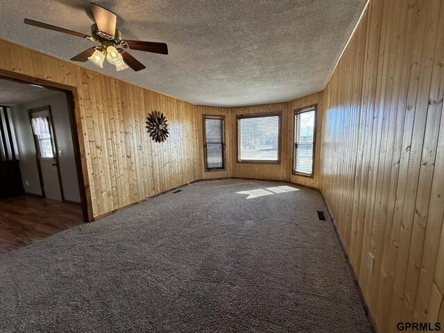108 S Quince Ave, Dewitt, NE 68341 - carpeted empty room featuring wooden walls, visible vents, a textured ceiling, and a ceiling fan