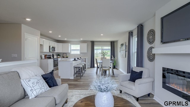 13607 Whitmore St, Omaha, NE 68142 - living room featuring light wood-type flooring, a glass covered fireplace, recessed lighting, and baseboards