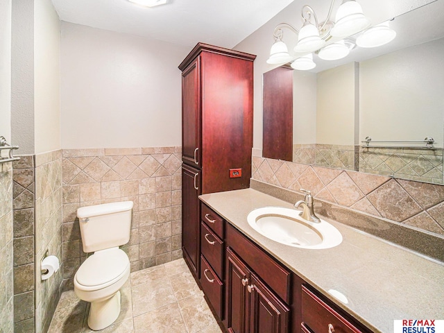bathroom with vanity, tile patterned flooring, a wainscoted wall, toilet, and tile walls