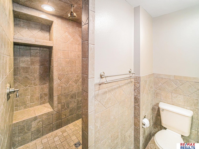 full bathroom with tiled shower, a wainscoted wall, tile walls, and toilet