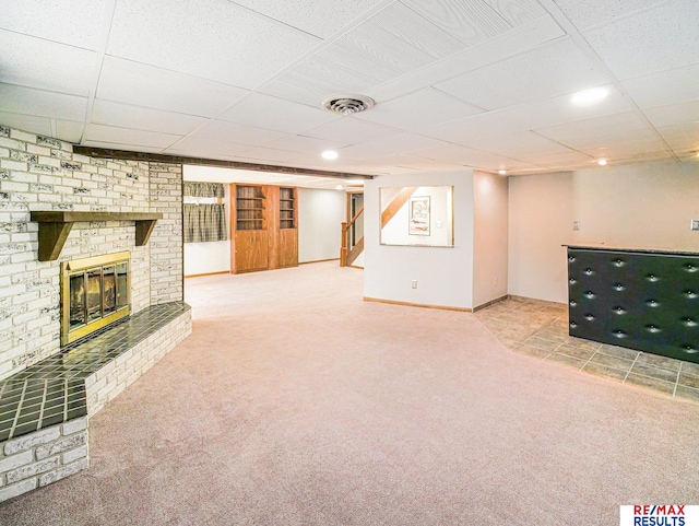 finished basement featuring a drop ceiling, visible vents, stairway, carpet flooring, and a brick fireplace