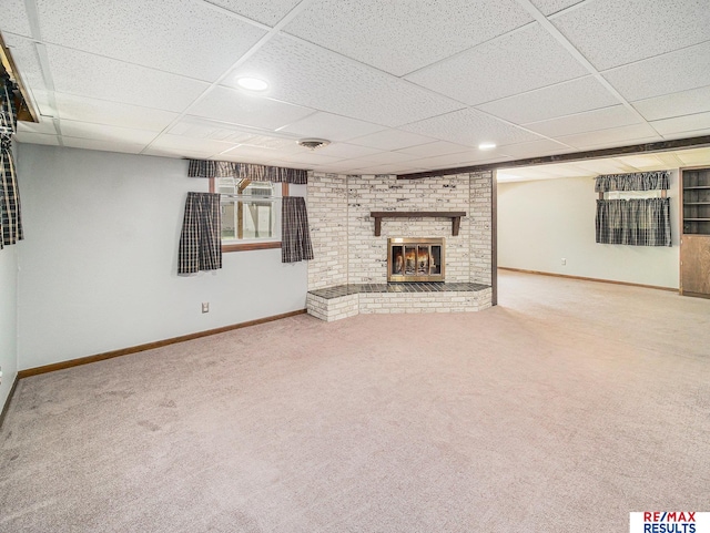 below grade area with baseboards, a drop ceiling, a brick fireplace, and carpet floors