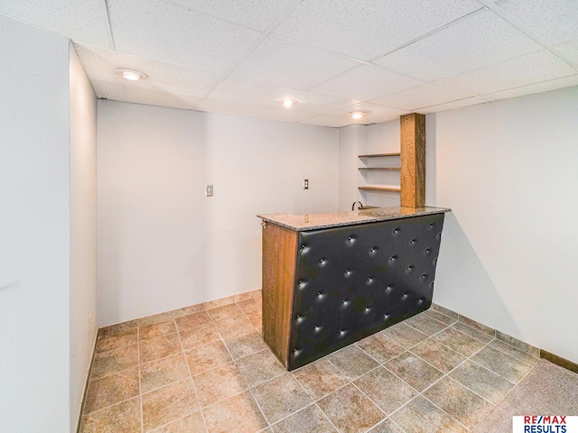 bar featuring a paneled ceiling, wet bar, and baseboards