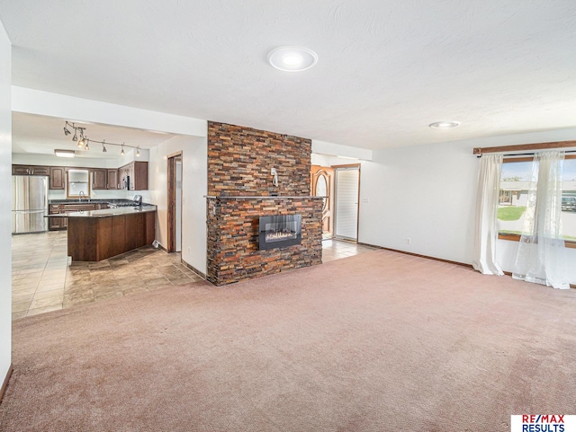 unfurnished living room featuring a stone fireplace, baseboards, light carpet, rail lighting, and a textured ceiling