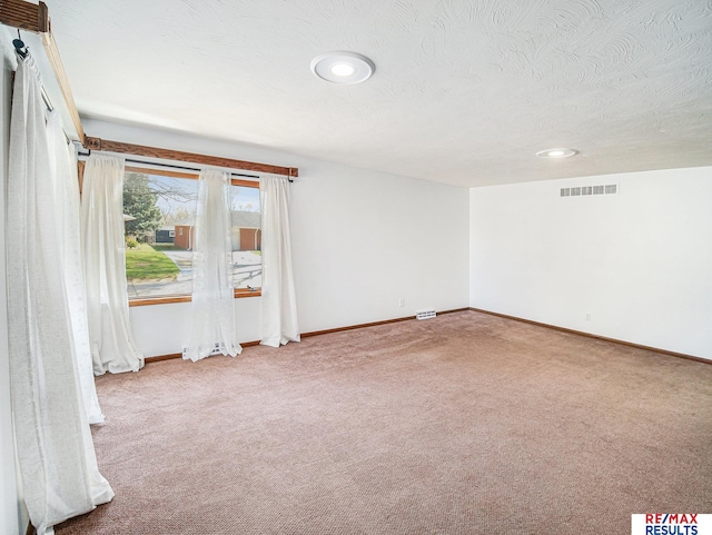 carpeted spare room with visible vents, baseboards, and a textured ceiling