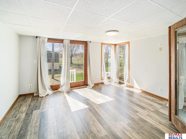 interior space with baseboards, a paneled ceiling, and wood finished floors