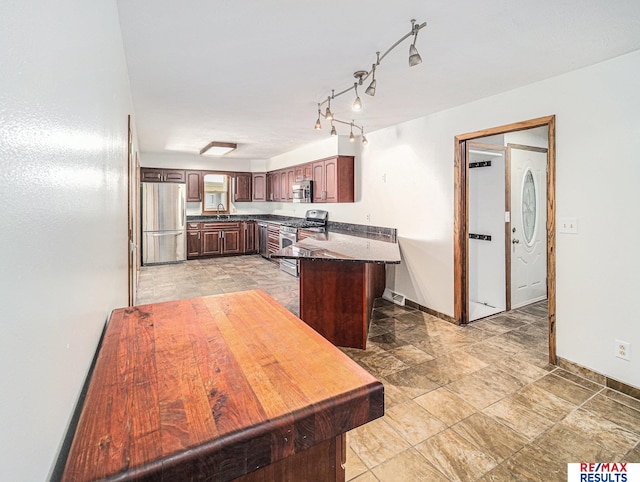 kitchen featuring baseboards, a peninsula, dark countertops, appliances with stainless steel finishes, and a sink