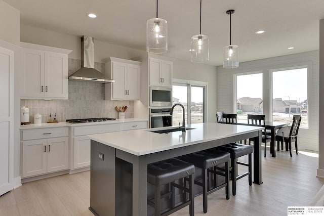 kitchen with gas stovetop, decorative backsplash, a sink, an island with sink, and wall chimney exhaust hood