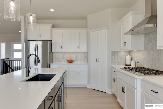 kitchen featuring light countertops, white cabinets, stainless steel appliances, a sink, and wall chimney range hood