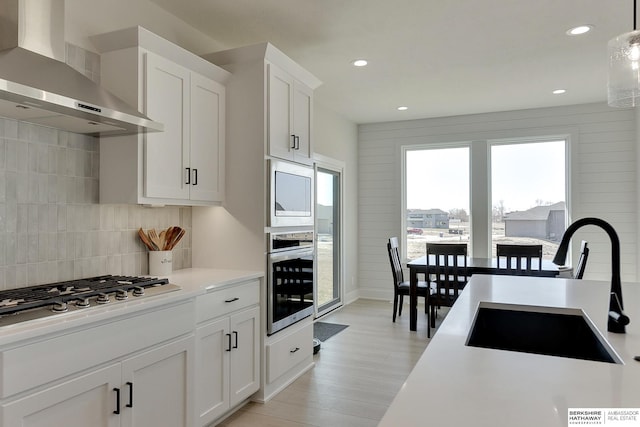 kitchen featuring light countertops, a sink, wall chimney exhaust hood, appliances with stainless steel finishes, and decorative backsplash