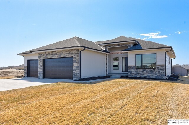 prairie-style home featuring an attached garage, stone siding, driveway, a front lawn, and a shingled roof