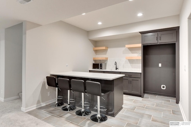 kitchen with light countertops, a sink, open shelves, a breakfast bar, and a peninsula