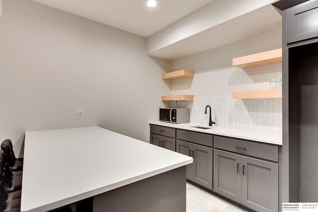 kitchen with a sink, open shelves, gray cabinets, and stainless steel microwave