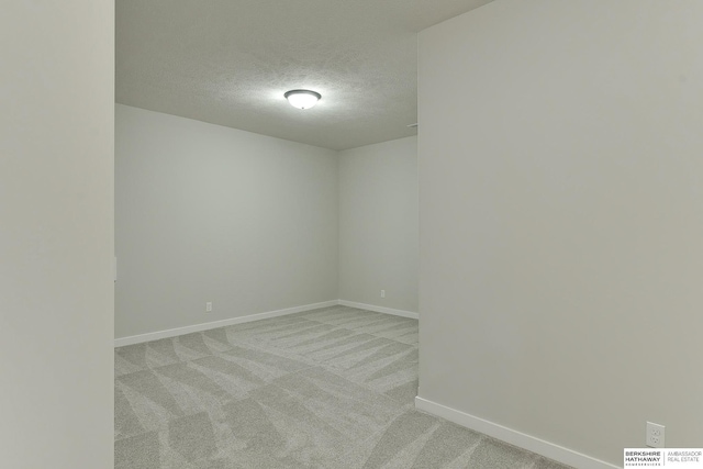 spare room featuring baseboards, a textured ceiling, and light colored carpet