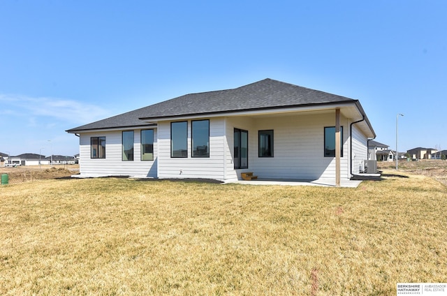 rear view of property featuring cooling unit, roof with shingles, and a lawn