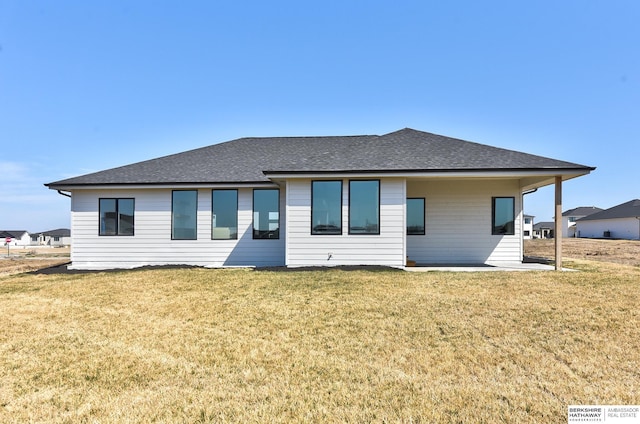 rear view of property with roof with shingles and a yard