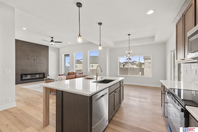 kitchen featuring a tray ceiling, a sink, light wood-style floors, and appliances with stainless steel finishes