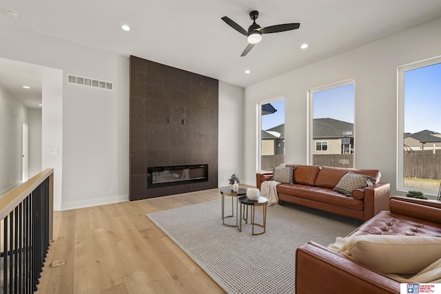 living area featuring a tiled fireplace, light wood-type flooring, visible vents, ceiling fan, and recessed lighting