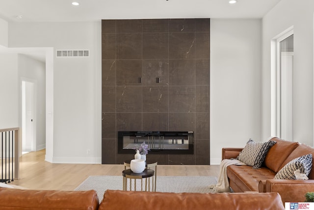 living room with a tile fireplace, wood finished floors, baseboards, visible vents, and recessed lighting