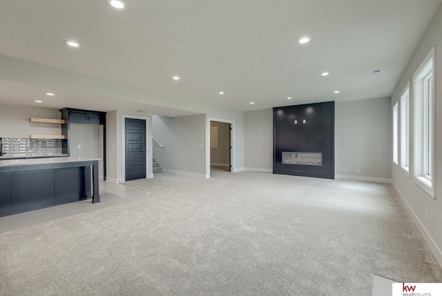 unfurnished living room featuring recessed lighting, light colored carpet, and stairway