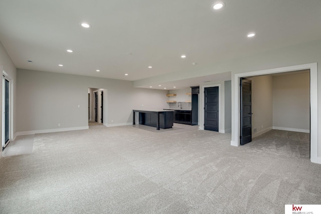 unfurnished living room featuring a sink, indoor bar, recessed lighting, and light colored carpet