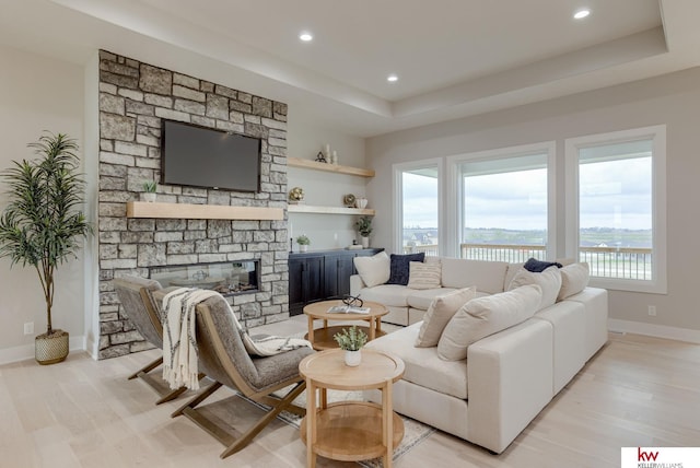 living room featuring recessed lighting, baseboards, a raised ceiling, and light wood-type flooring