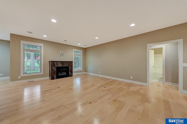 unfurnished living room featuring baseboards, a tiled fireplace, light wood-style flooring, and recessed lighting