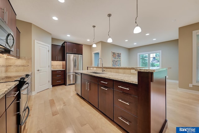 kitchen with backsplash, a sink, appliances with stainless steel finishes, a center island with sink, and light wood-type flooring
