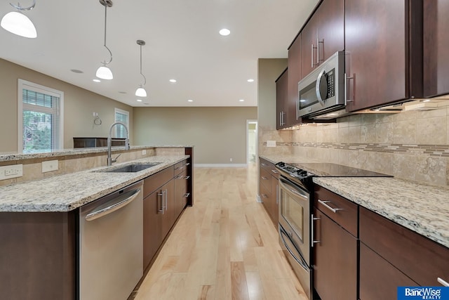 kitchen featuring stainless steel appliances, backsplash, hanging light fixtures, a sink, and light wood-style flooring