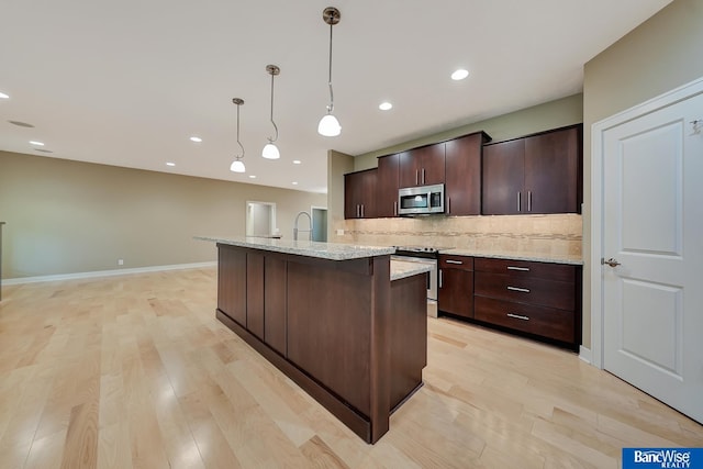 kitchen with a kitchen island with sink, light wood-type flooring, tasteful backsplash, and appliances with stainless steel finishes