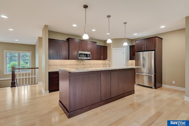 kitchen with backsplash, an island with sink, light wood finished floors, dark brown cabinetry, and appliances with stainless steel finishes