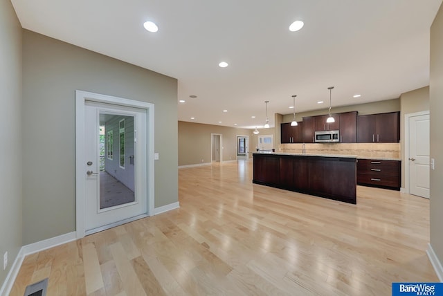 kitchen with dark brown cabinetry, tasteful backsplash, open floor plan, light wood-style flooring, and stainless steel microwave