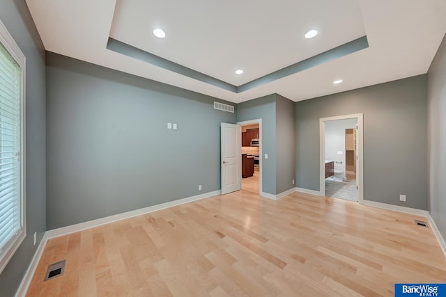 unfurnished bedroom featuring a tray ceiling, light wood-style floors, and visible vents