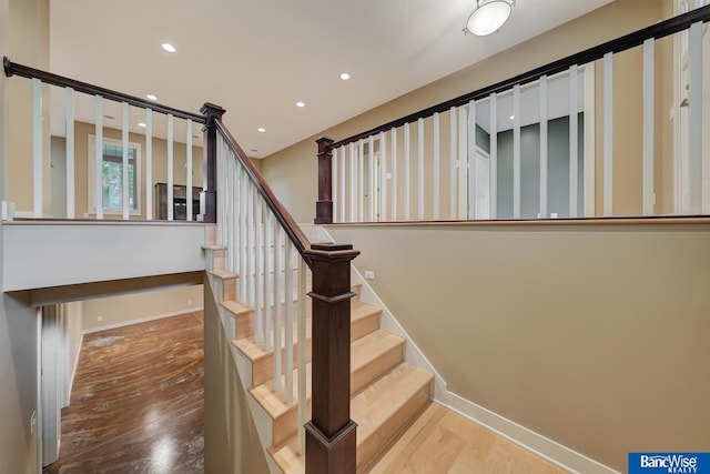 stairs with baseboards, wood finished floors, and recessed lighting