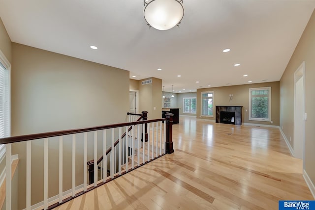 hall featuring an upstairs landing, light wood-type flooring, baseboards, visible vents, and recessed lighting