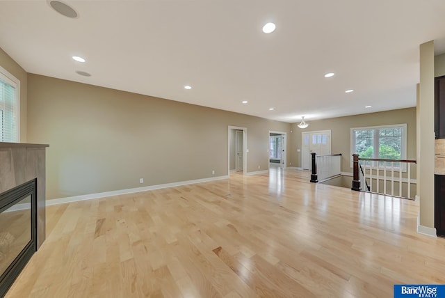 unfurnished living room featuring baseboards, a glass covered fireplace, recessed lighting, and light wood finished floors