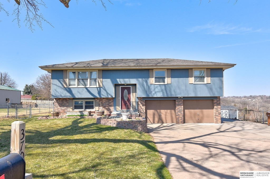 bi-level home featuring driveway, an attached garage, fence, brick siding, and a front lawn