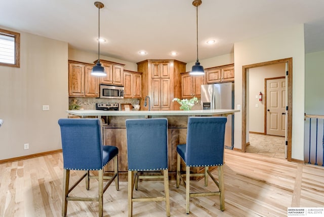 kitchen featuring appliances with stainless steel finishes, a breakfast bar area, brown cabinets, and recessed lighting