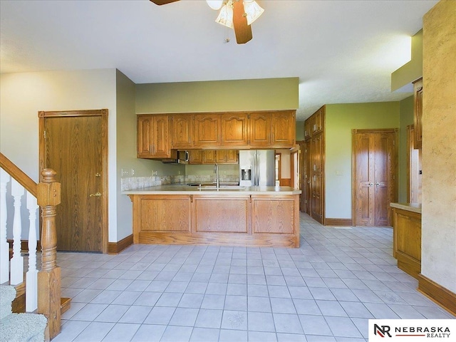 kitchen with light countertops, a peninsula, ceiling fan, brown cabinets, and stainless steel refrigerator with ice dispenser