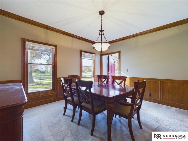 dining area featuring a wainscoted wall, ornamental molding, and light carpet