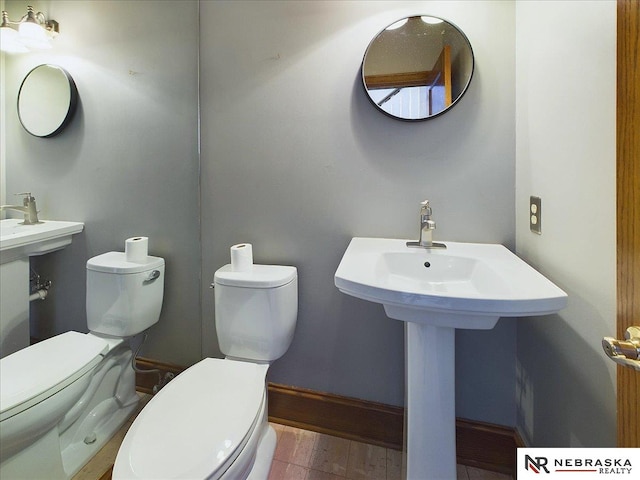 bathroom with baseboards, wood finished floors, toilet, and a sink